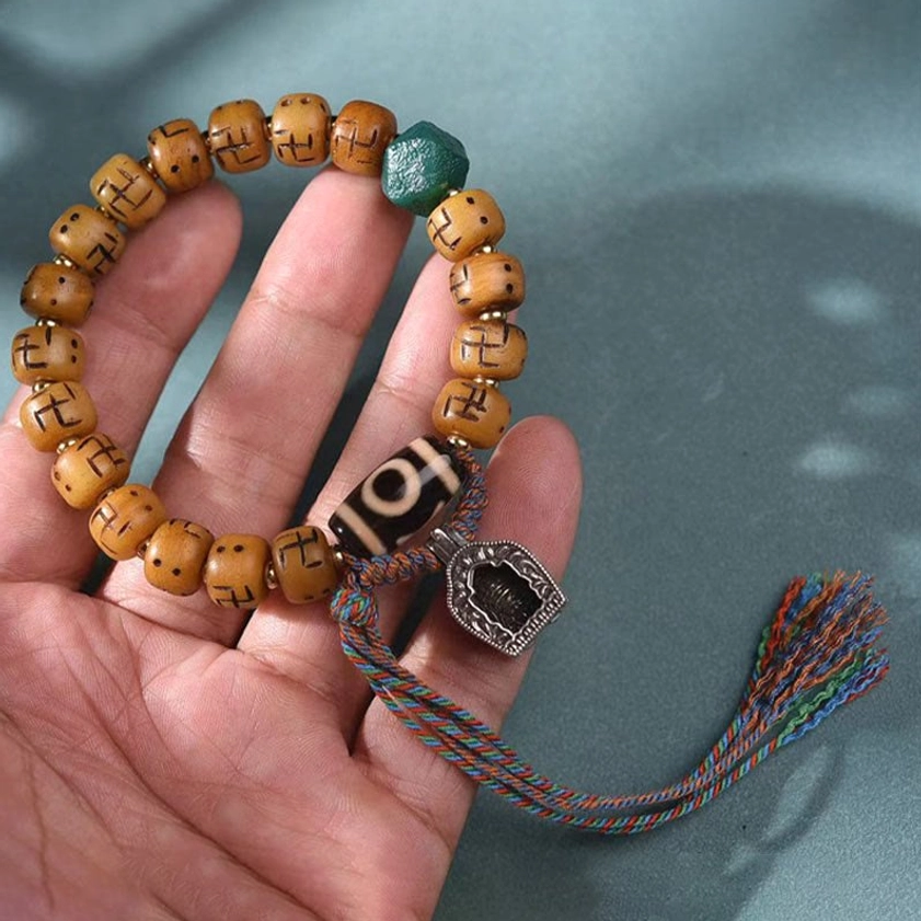 Buddhist camel bone prayer bracelet held in hand showing size, dzi bead, metal charm, and tassel detail