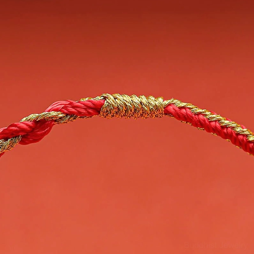 Gold woven wrapping knot and red twisted rope closure detail of handmade Buddhist bracelet