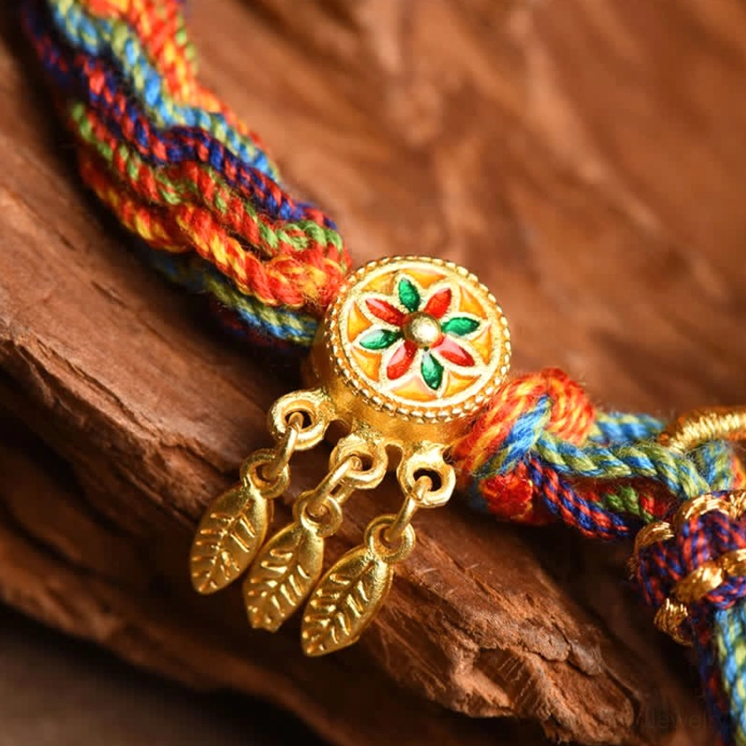 Close-up of Buddhist bracelet decorative elements showing enamel flower ornament and gold leaf pendants
