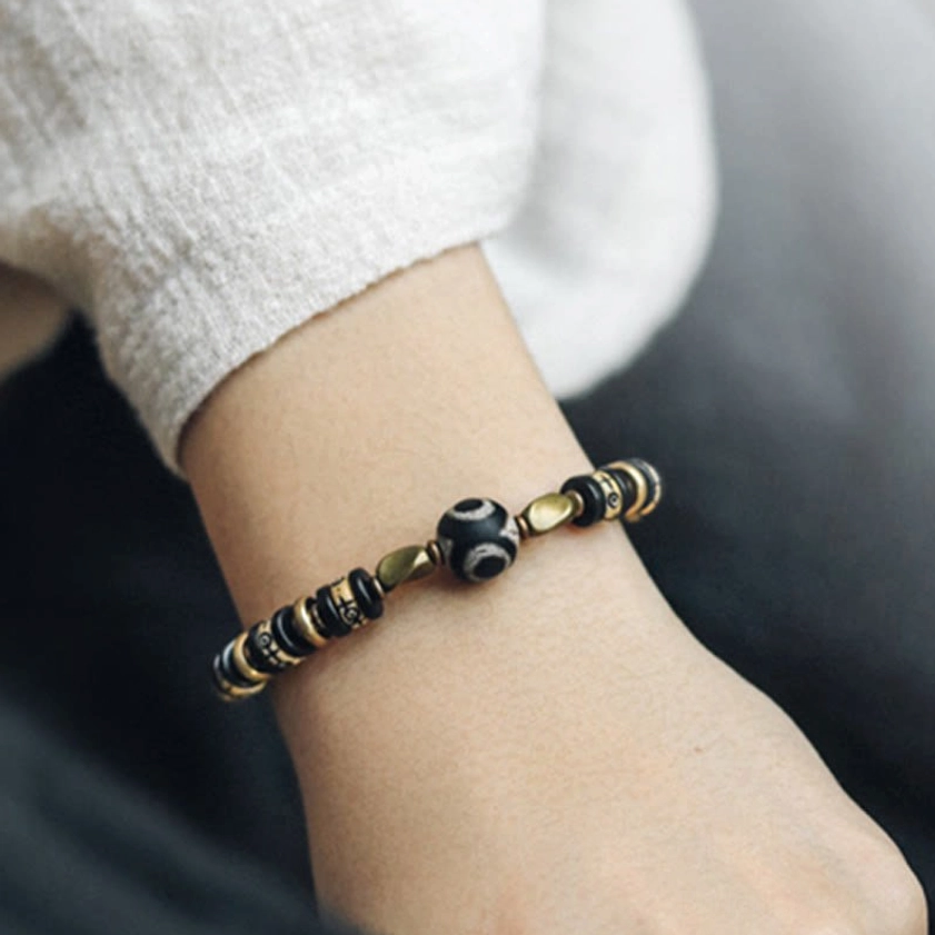 Close-up side view of Buddhist strength bracelet showing engraved symbol beads, Dzi centerpiece, and minimalist design on wrist