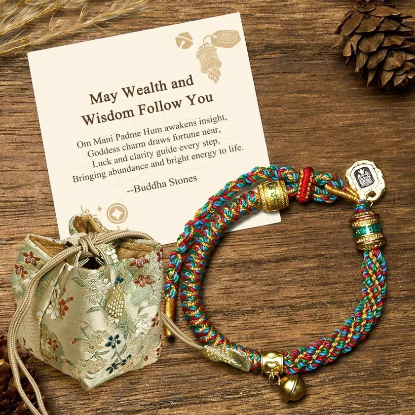 Multicolor Buddhist bracelet with deluxe embroidered gift bag, greeting card, and metal bell charm displayed on wooden desktop with nature elements