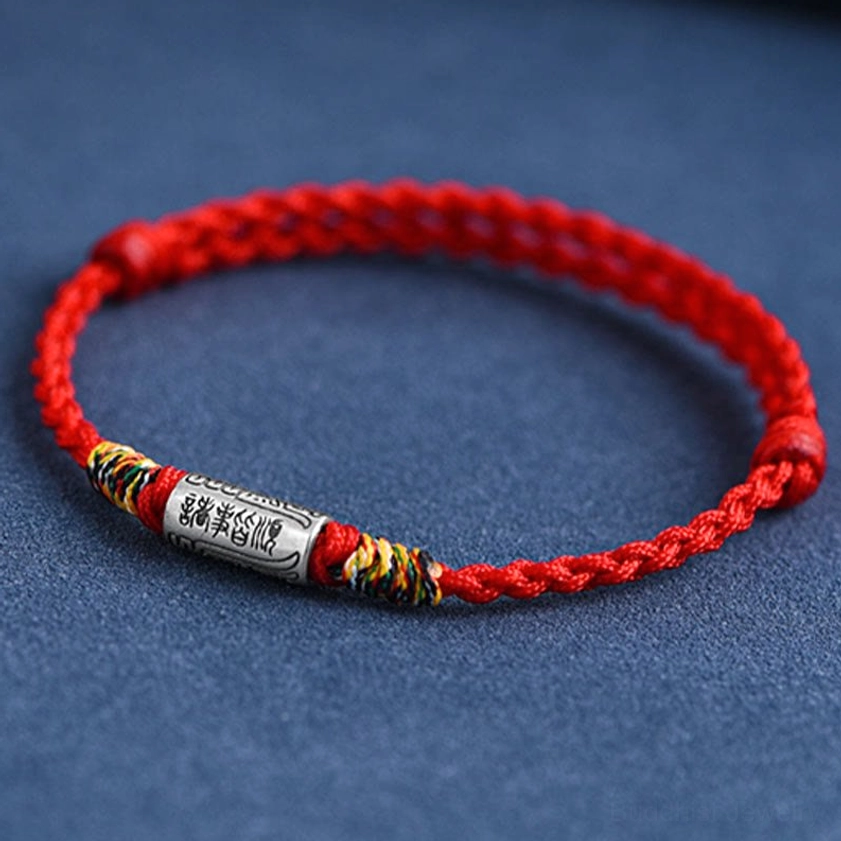 Close-up of engraved silver charm tube on Buddhist blessing bracelet, showing clear spiritual characters, oblique top view with braided rope base
