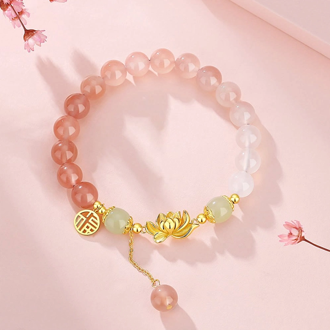 Top view of beaded Buddhist bracelet featuring red gradient agate, gold lotus and Fu character charms with hanging tassel