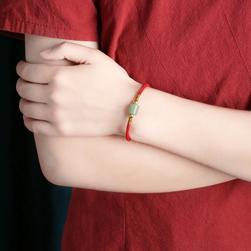 Worn on wrist close-up view of Buddhist red string bracelet with green aventurine charm and gold hardware