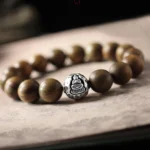 Green sandalwood and sterling silver Buddhist bracelet with engraved Buddha charm, top-down view showing smooth wooden beads and matte silver detail