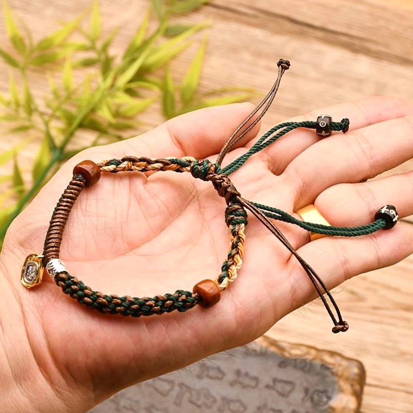 Hand-held Buddhist bracelet in earthy green-brown tones with adjustable drawstring, featuring wooden beads and spiritual charm pendant