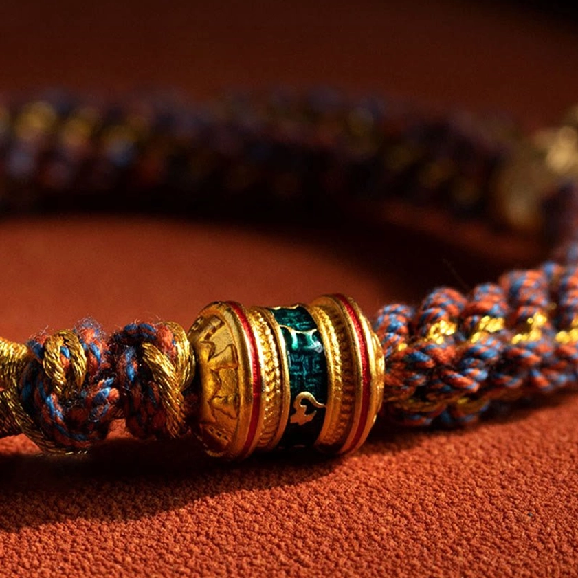 Close-up detail of enamel-inlaid metal beads and twisted cord texture in Buddhist red string bracelet