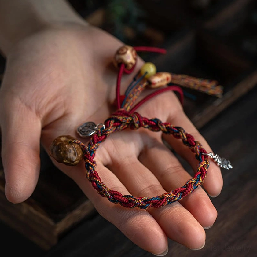 Buddhist protection bracelet held in palm showing multicolor braided cords, silver charms, mixed beads and tassel trim, close-up detail shot