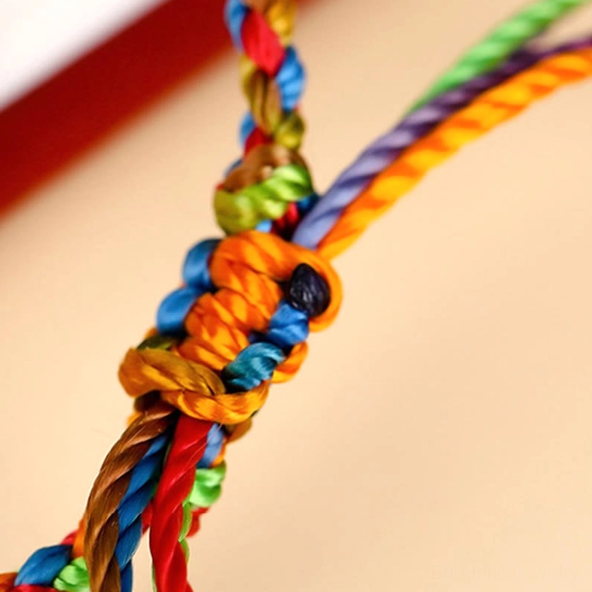 Side angle of handmade Buddhist bracelet knot showing intricate multi-strand weave with bright rainbow colors