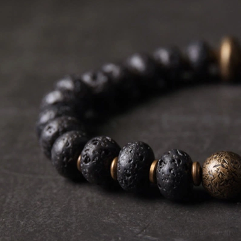 Overhead close-up detail of Buddhist lava rock copper bracelet with porous black beads and ornate metal accent