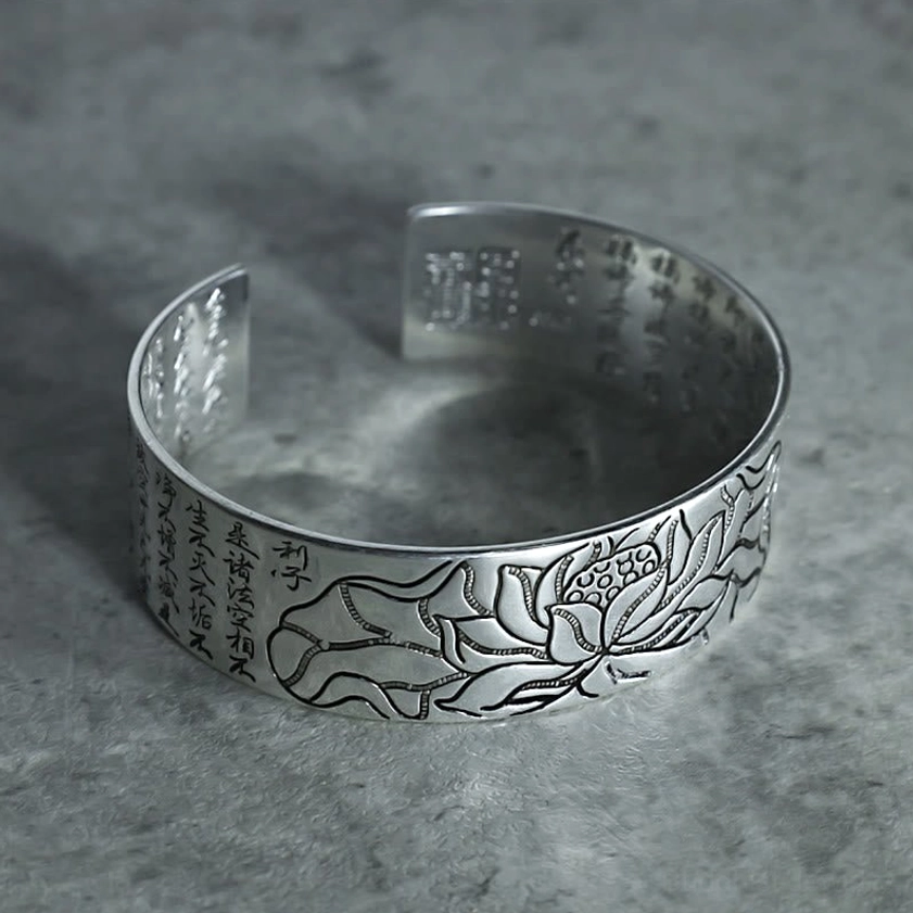 White copper open cuff bracelet overhead top view displaying carved lotus motif and full Buddhist sutra engravings on outer surface