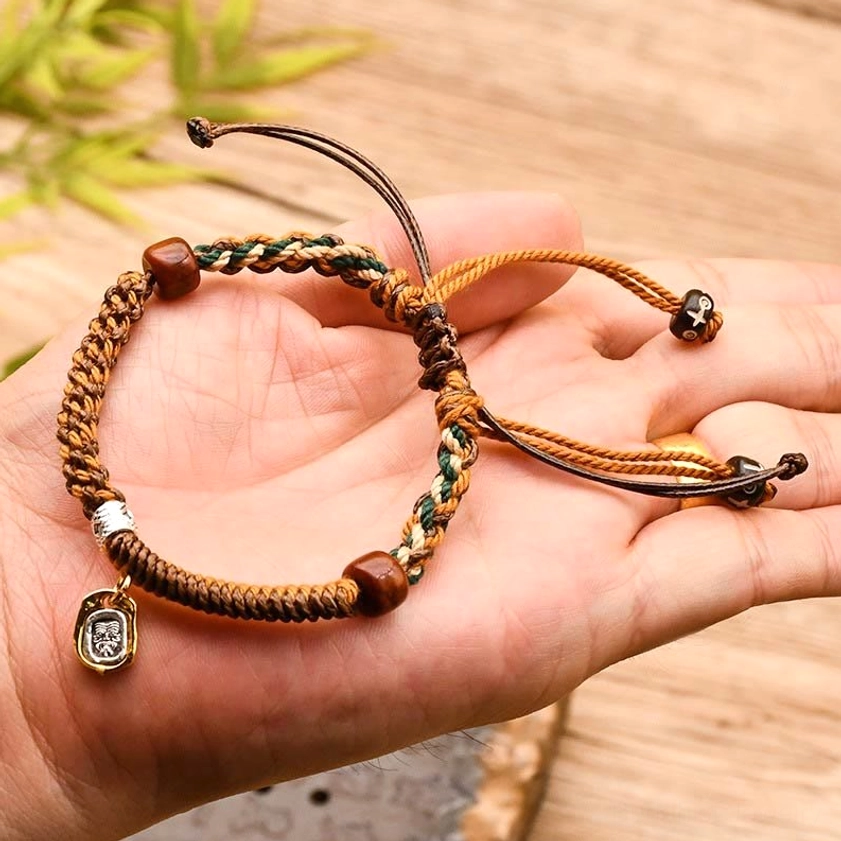 Close-up palm view of Buddhist red string protection bracelet with wooden beads and metal charm pendant, handmade artisan craft