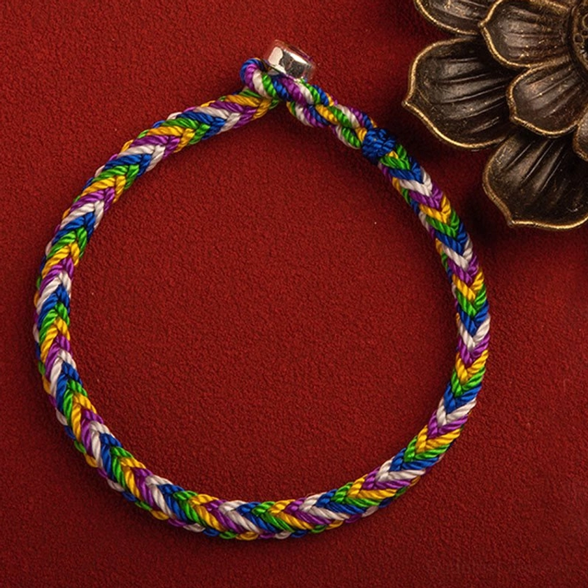 Colorful Buddhist lucky bracelet with silver clasp detail, flat lay on red background with bronze flower decoration