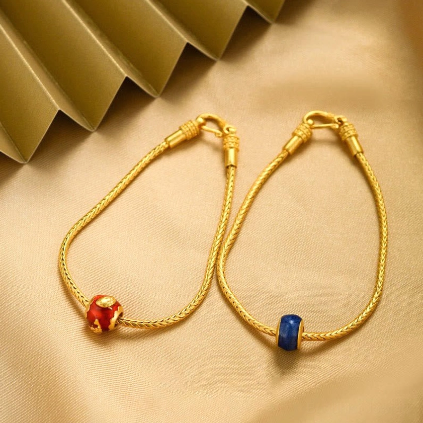 Two Buddhist gold bracelets with red and blue enamel bead charms on twisted chain