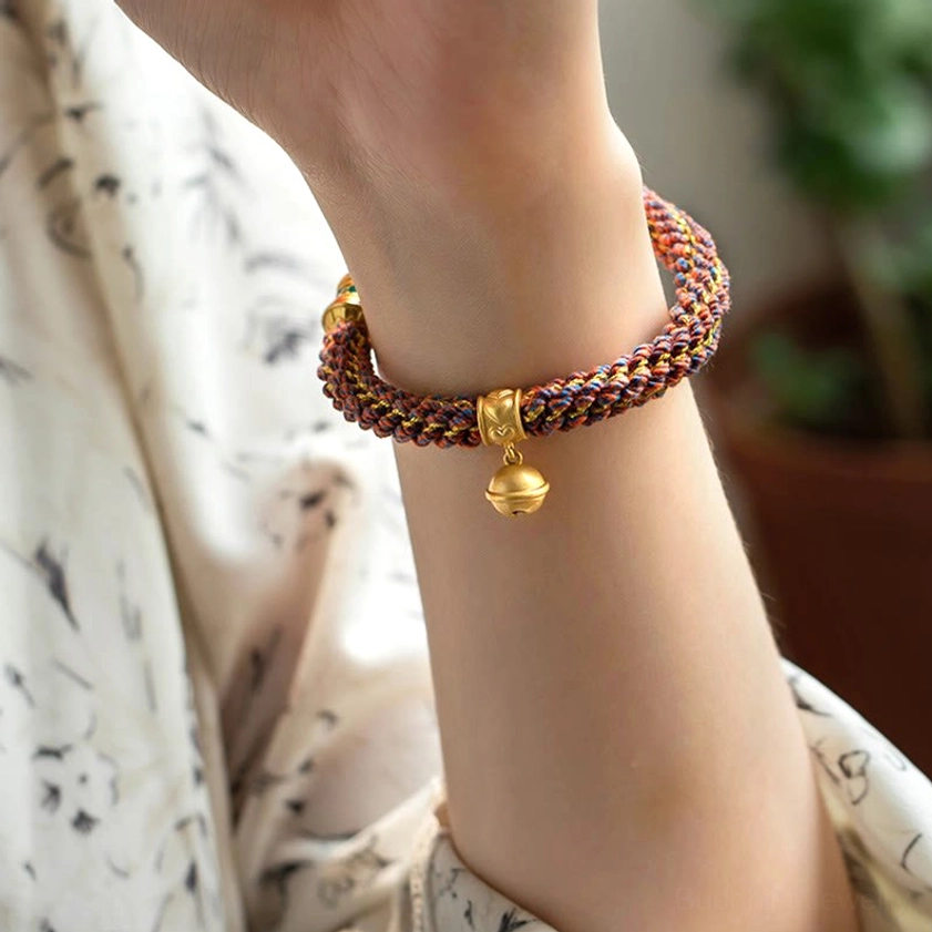 Side view of handwoven Buddhist bracelet on wrist highlighting brass bell charm and protective cord