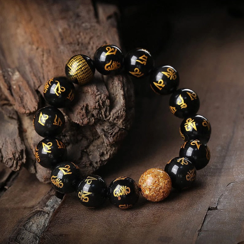 Handcrafted obsidian mantra bracelet with glossy black beads engraved with golden Sanskrit characters and premium gold foil accent bead, oblique side angle
