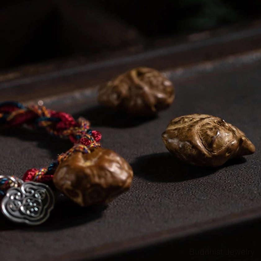 Close-up detail of Buddhist protection bracelet showing red braided ropes, silver Ruyi charm, large natural stone bead accents on metal tray