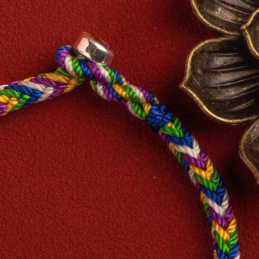 Buddhist lucky bracelet silver clasp and braided thread junction, close-up side view with bronze ornament accent