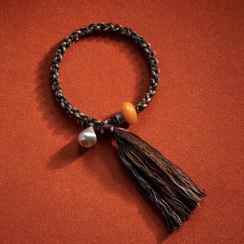 Flat lay 990 sterling silver amber protective bracelet with tassel charm on solid red background