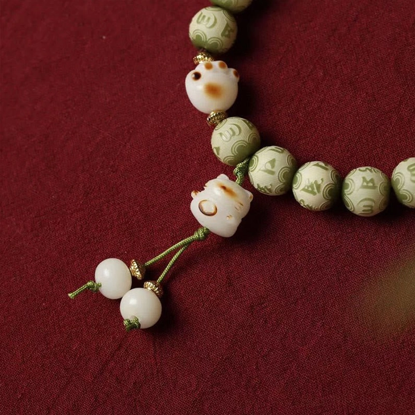 Detailed view of Bodhi seed bracelet tassel and cat paw pendants with bead accents on red textile