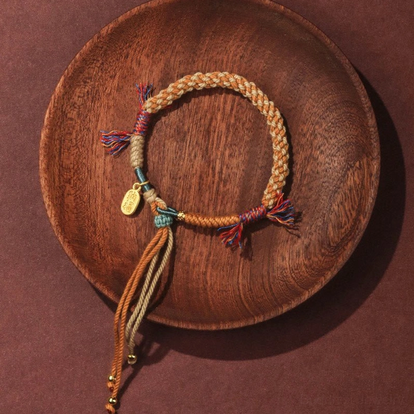 Side view of adjustable Buddhist string bracelet showing twisted braided design, hanging tassels, and engraved Fu pendant charm