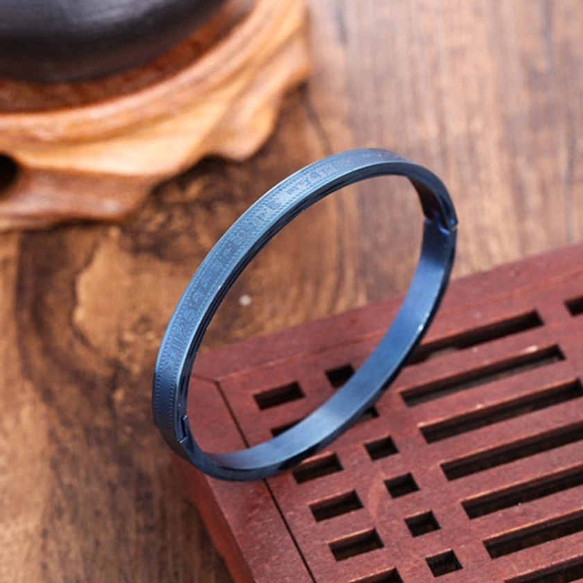 Burnt blue titanium steel Buddhist blessing bracelet with engraved decorative patterns on cuff, displayed on red wood tray