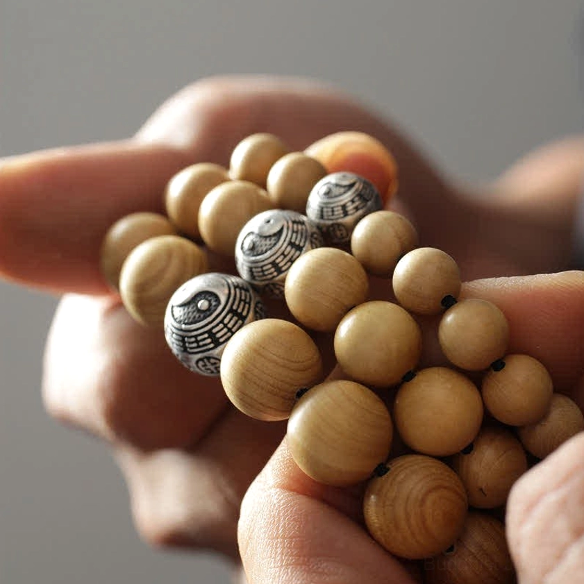 Close-up of handcrafted Buddhist bracelet with engraved silver charm beads held in palm showing natural wood texture