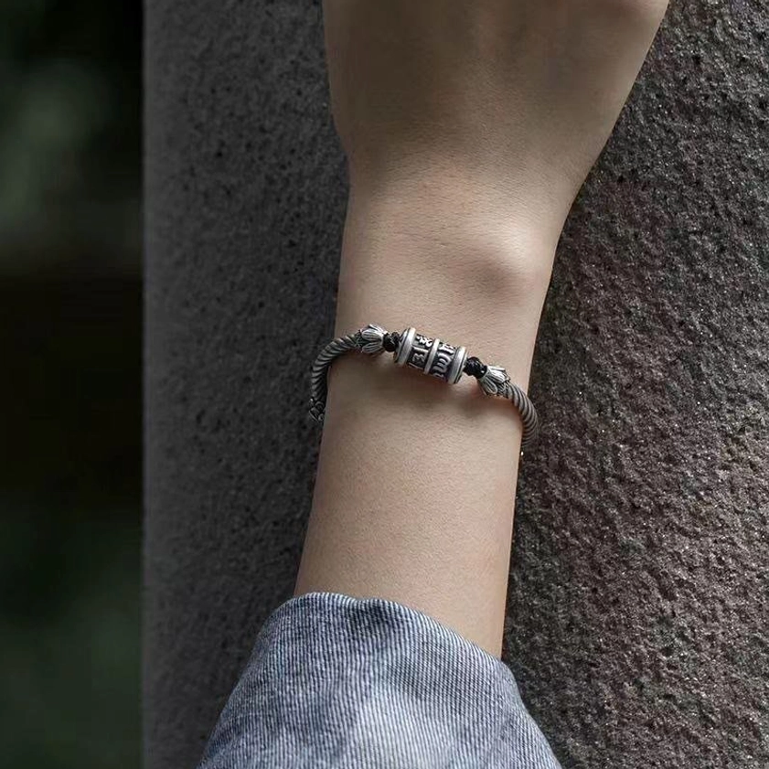 Lotus peace bracelet on slim wrist against concrete wall, demonstrating adjustable fit and delicate tibetan mantra design