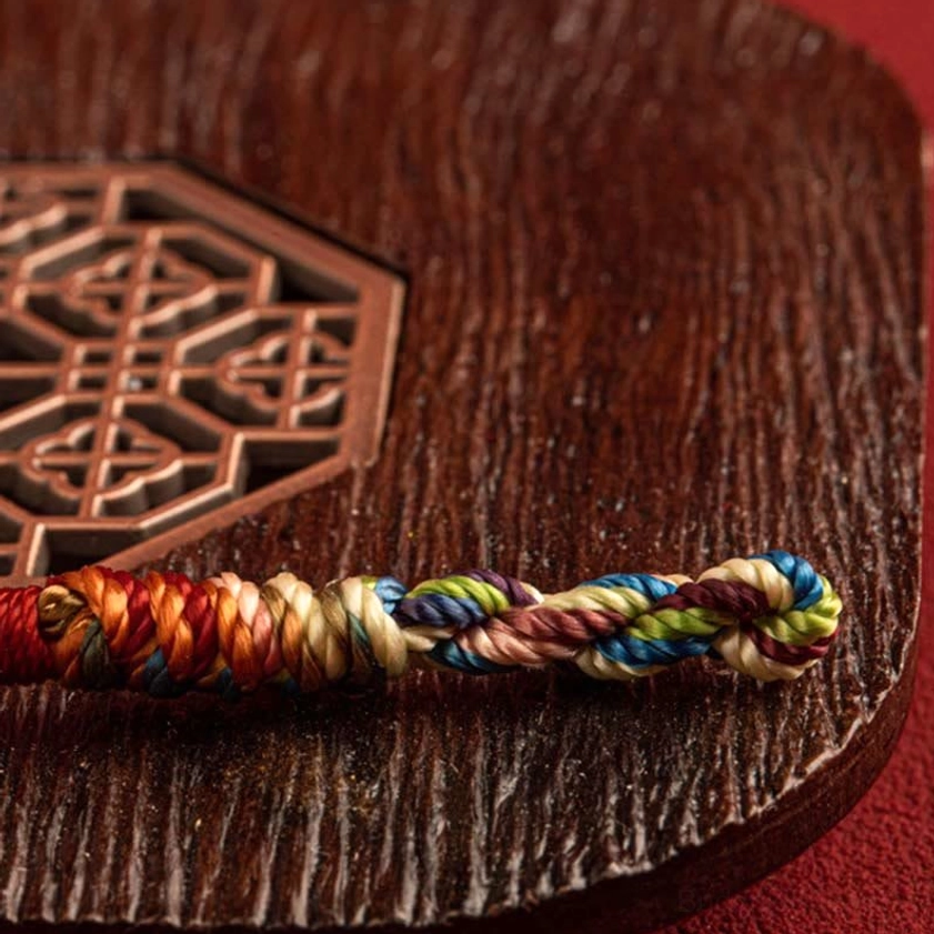 Buddhist string bracelet sample on wooden carved surface showing multicolored twisted weave and knot work