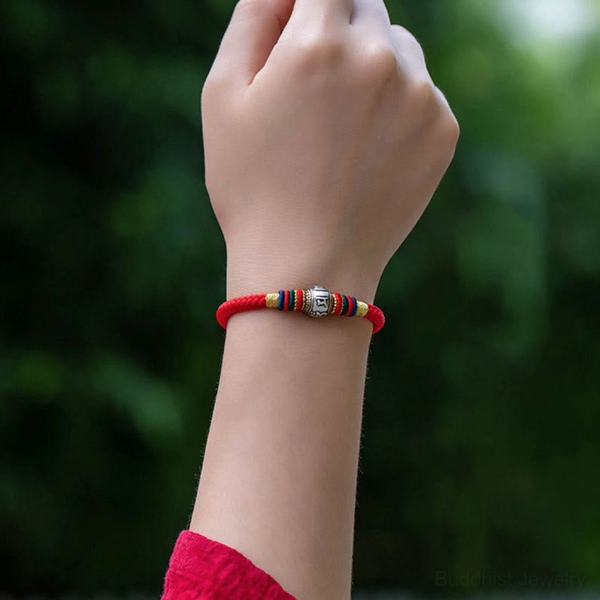 Woman wearing red Om Mani Padme Hum Buddhist bracelet on wrist outdoors with green foliage background, close-up side view