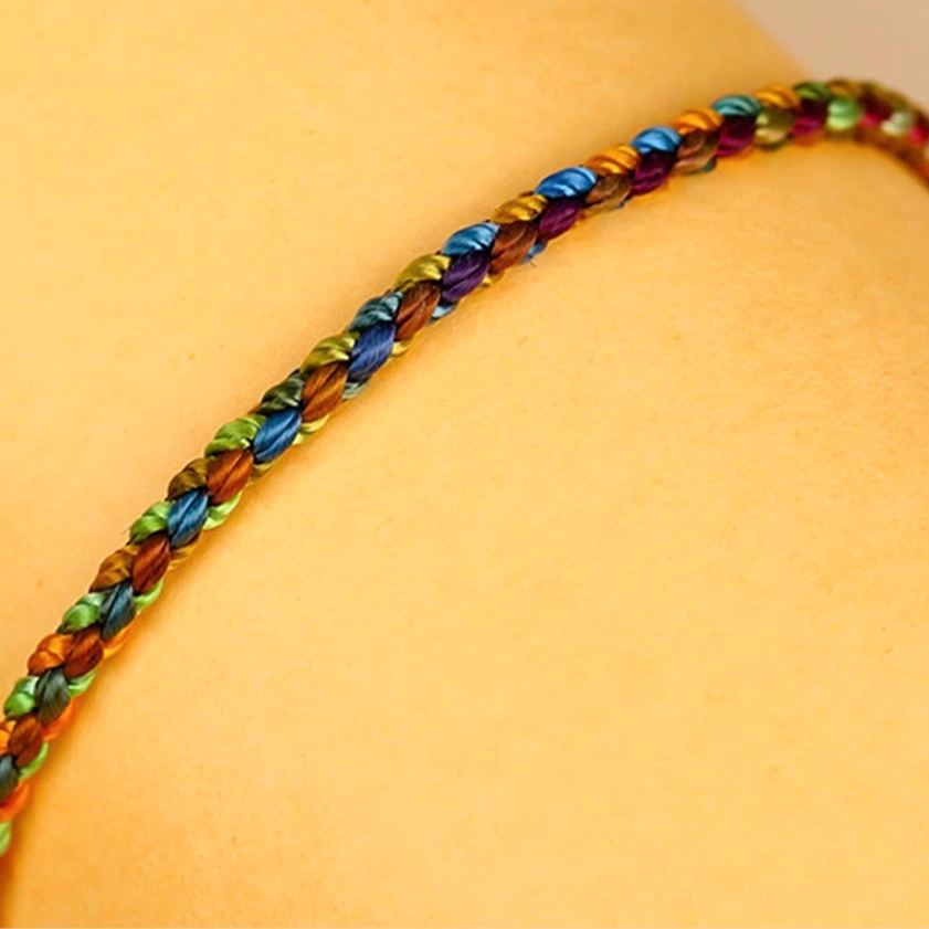 Closeup flat lay of multicolored Buddhist bracelet section displaying neat woven texture and mixed rainbow silk threads