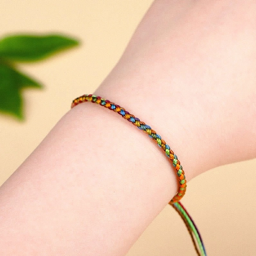 Rainbow Buddhist string bracelet on wrist with natural trailing rope end detail and green leaf background