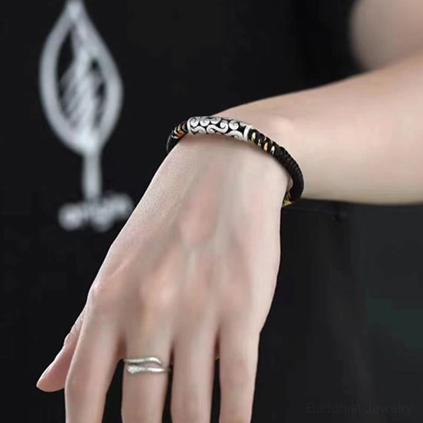 Handmade Buddhist string bracelet worn on wrist with silver ring, showing adjustable fit and detailed craftsmanship on light skin tone