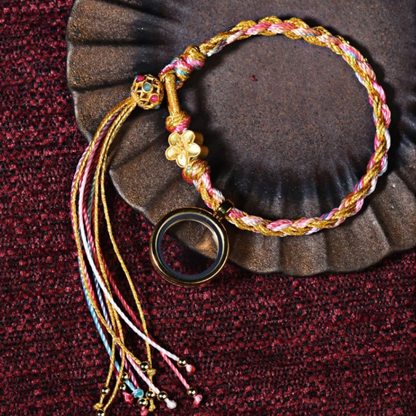 Buddhist lucky braided string bracelet with pink-gold multicolor braid, gold flower charm and metal hanging ring on antique background