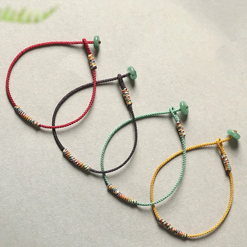 Set of four Buddhist string bracelets in assorted colors with green aventurine charms and braided woven accents, flat lay arrangement