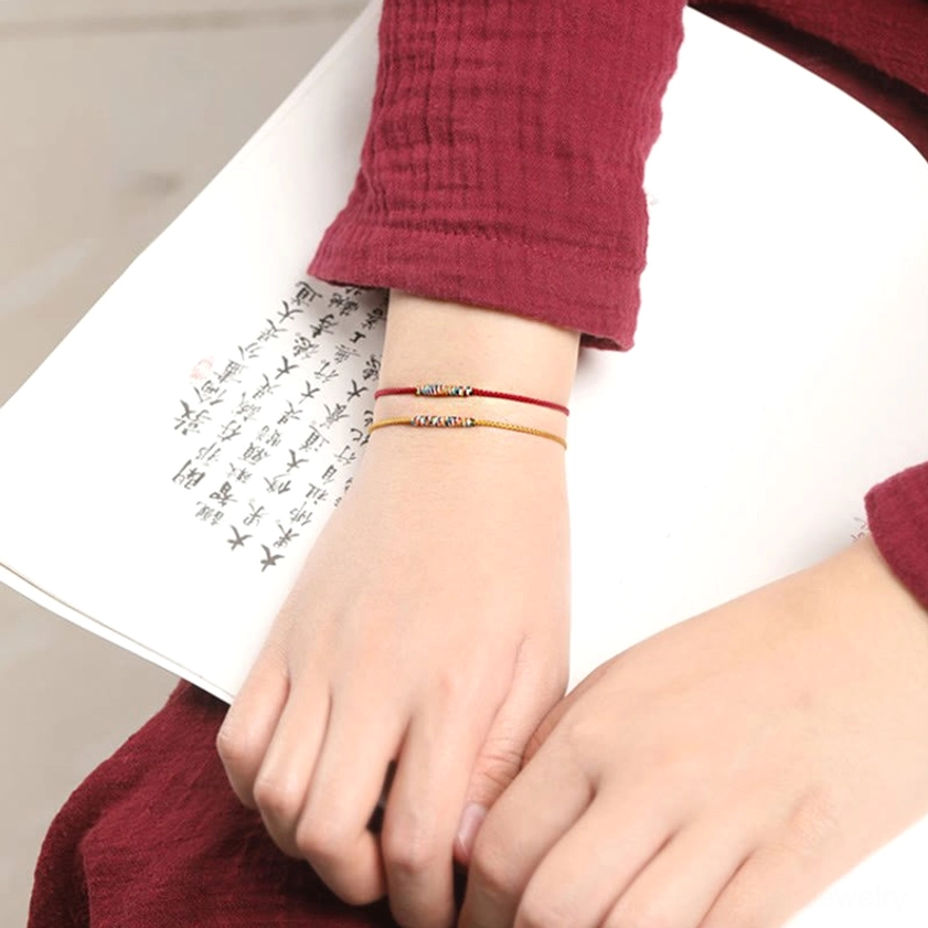 Minimalist Buddhist braided bracelets in red and yellow worn on forearm with Chinese calligraphy book backdrop, spiritual practice styling