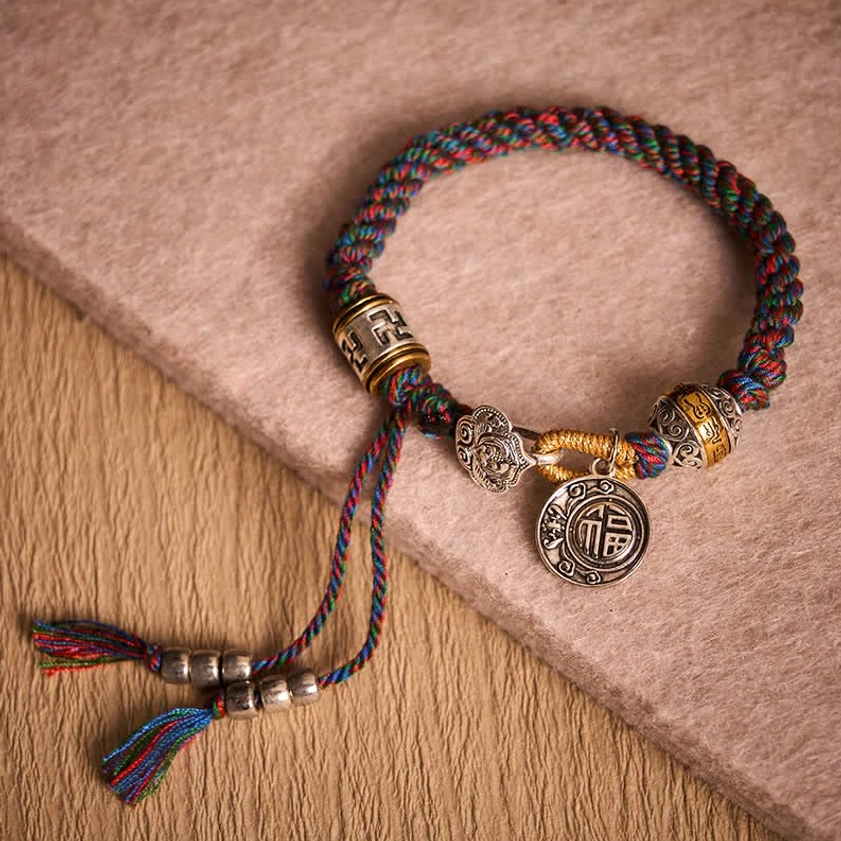 Handcrafted Buddhist String Bracelet with Silver Charms and Multicolor Woven Rope on Fabric Surface