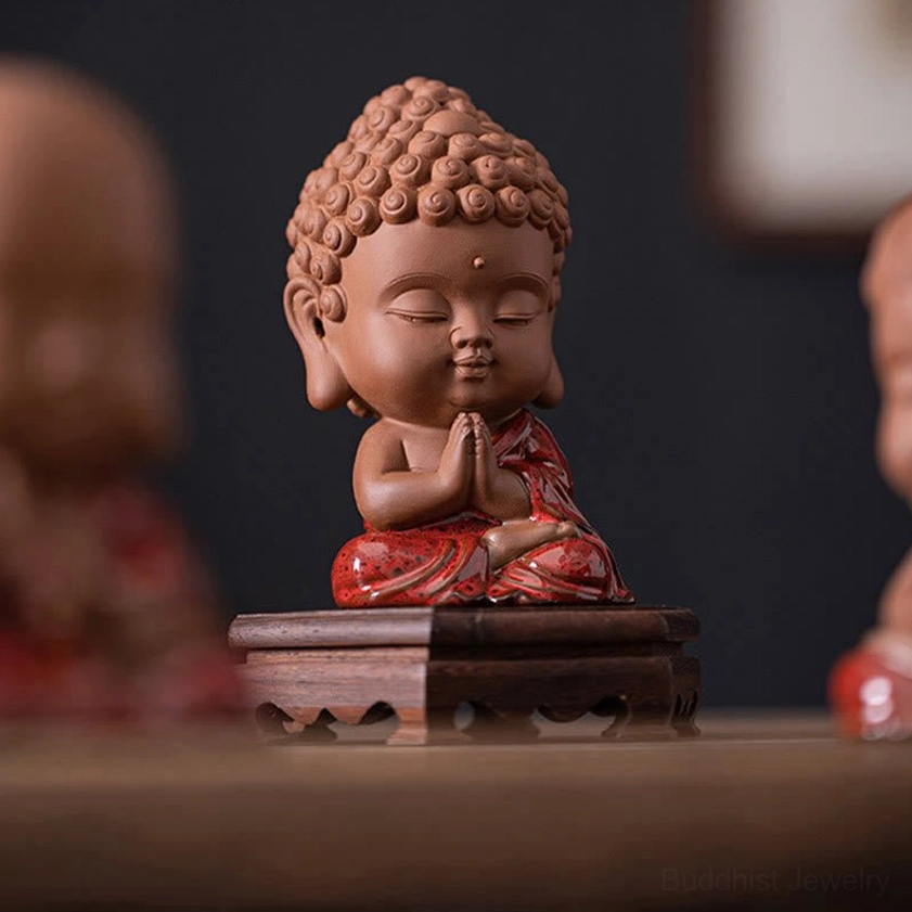 Front eye-level perspective of mini Buddhist Buddha figurine with prayer hands gesture, terracotta finish, and red glazed details on wooden display