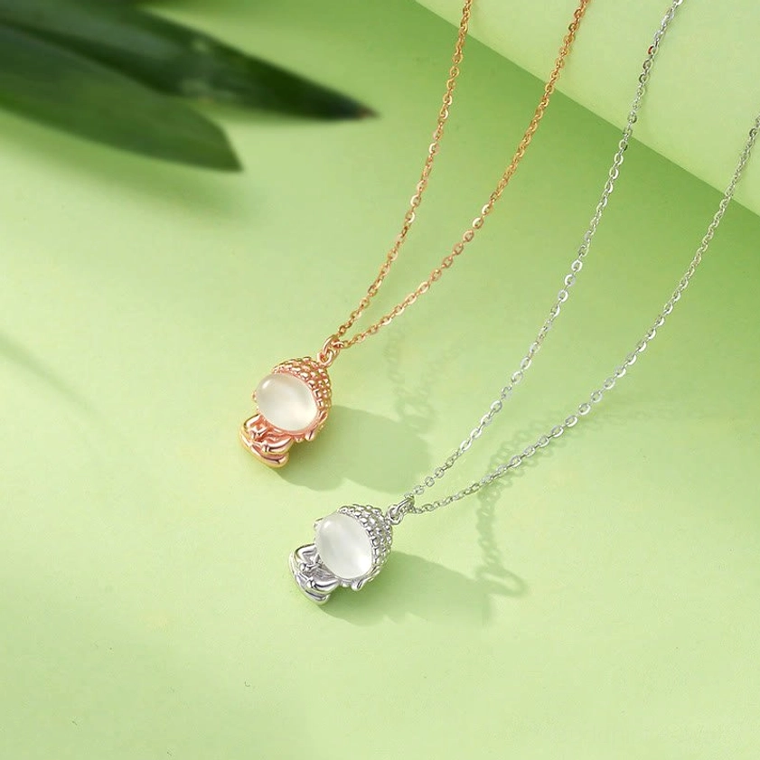 Pair of Buddhist pendant necklaces in rose gold and silver tone with matching chalcedony Buddha charms on thin cable chains, flat lay overhead view