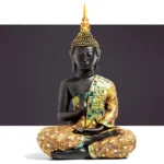 Hand-carved black resin Buddha statue with gold and teal embroidered robe in prayer mudra pose, frontal view on gray background