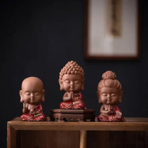 Three handcrafted Buddhist ceramic figurines - Sakyamuni Buddha, Avalokitesvara Guan Yin, and Ksitigarbha - displayed together on wooden shelf with terracotta and red glazed robe details