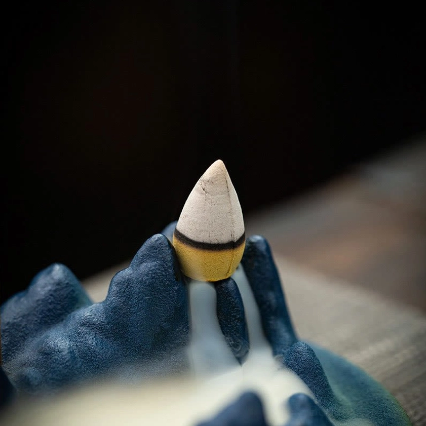 Close-up three-quarter view of handcrafted ceramic Buddhist incense holder with brown-white incense cone installed and backflow smoke effect