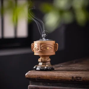 Yellow Buddhist ceramic incense burner with golden relief design, front view on wooden desk with natural foliage background