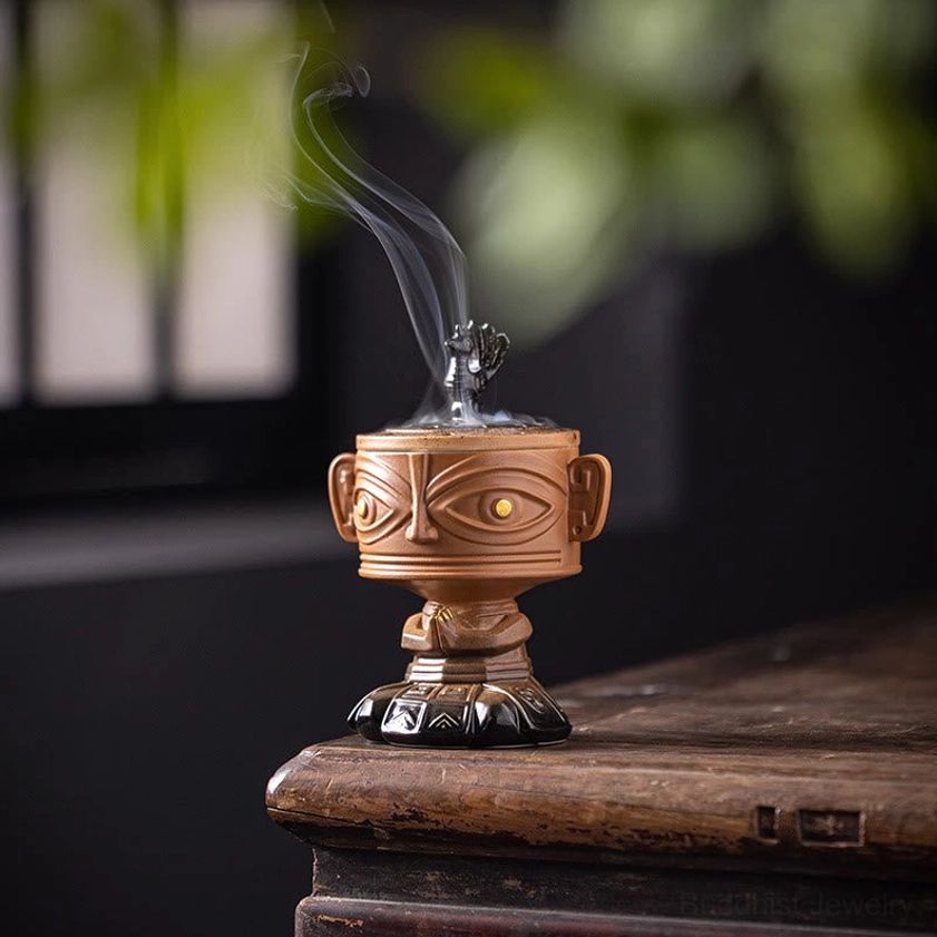 Yellow Buddhist ceramic incense burner with golden relief design, front view on wooden desk with natural foliage background