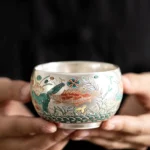 Handcrafted Buddhist enameled ceramic kung fu tea cup with auspicious fish and lotus aquatic design, silver interior close-up view
