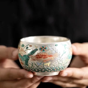 Handcrafted Buddhist enameled ceramic kung fu tea cup with auspicious fish and lotus aquatic design, silver interior close-up view