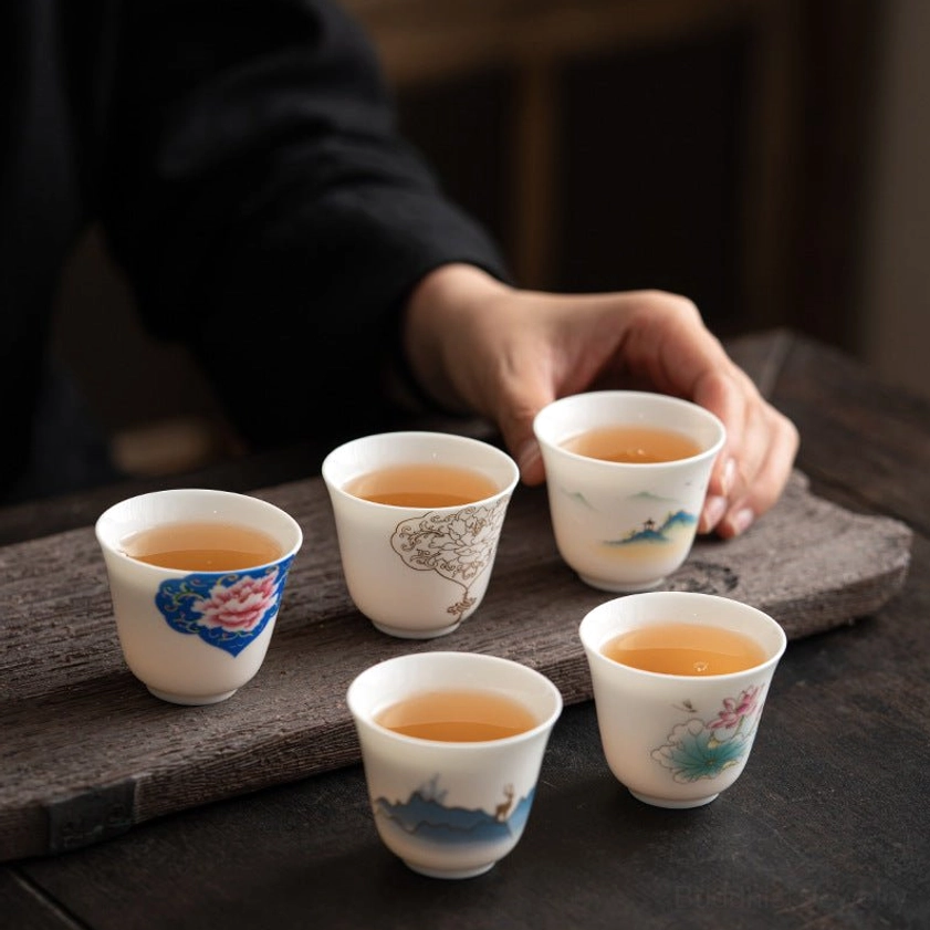 Set of 5 handmade Buddhist porcelain kung fu tea cups with traditional hand-painted designs including lotus, peony, and landscape patterns, top view with brewed tea