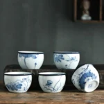 Handcrafted blue and white ceramic Buddhist tea cups with lotus and landscape patterns, overhead flat lay display on wooden table