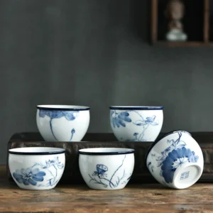 Handcrafted blue and white ceramic Buddhist tea cups with lotus and landscape patterns, overhead flat lay display on wooden table