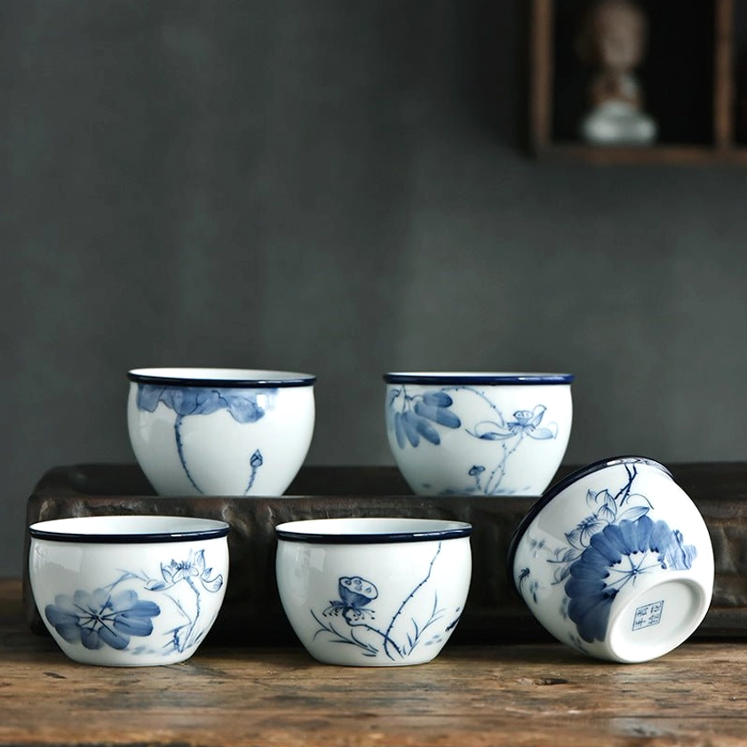 Handcrafted blue and white ceramic Buddhist tea cups with lotus and landscape patterns, overhead flat lay display on wooden table